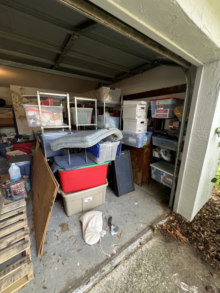 Garage entrance filled with storage bins, metal shelving, and a rolled floor covering.
